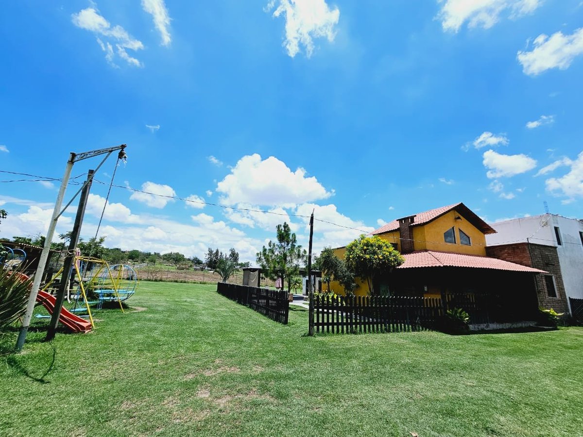 Casa de campo rural con exterior amarillo, cerca de madera y columpio en amplio jardín verde
