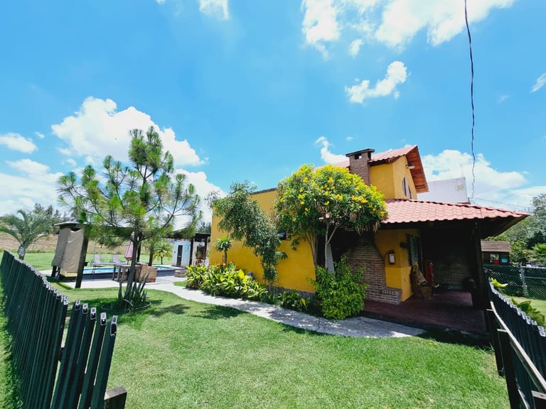 Casa colonial amarilla con techo rojo rodeada de jardines y palmeras